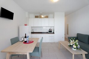 A compact living space with a dining table, chairs, a sofa, a kitchenette, and a flat-screen TV.