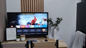 A television displaying a movie, a framed picture, a small plant, and a chair. - Mall Of Asia - Aseana Shore Residences (Pasay)