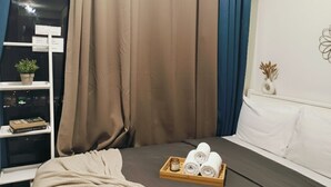A hotel room with a bed, a tray with towels, a shelf with a plant, and a wall with a decorative item. - Mall Of Asia - Aseana Shore Residences (Pasay)