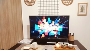 A dining area with a TV, table, chairs, placemats, a candle, and a decorative basket. - Mall Of Asia - Aseana Shore Residences (Pasay)