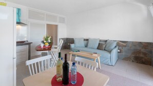 Een compacte leefruimte met kitchenette, een eethoek en een zithoek met een bank en stoelen.