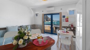 Een eetruimte met een tafel, stoelen, een bloemstuk en uitzicht op de zee door een glazen deur.