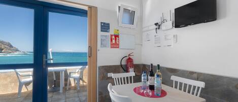 Una habitación con una mesa de comedor, sillas, un televisor de pantalla plana, un extintor y vistas al mar.