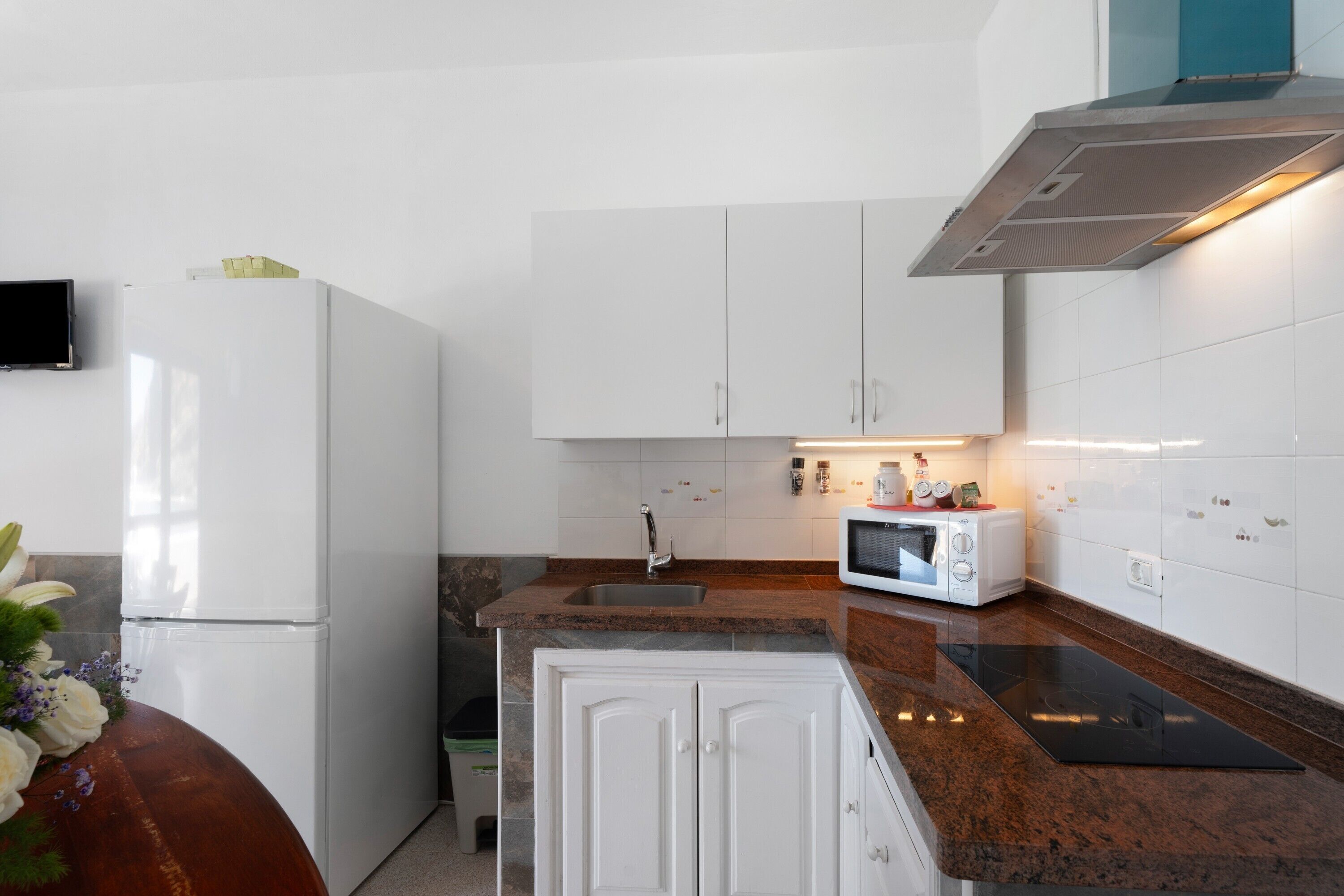 Una cocina moderna con gabinetes blancos, un microondas integrado y una campana extractora de acero inoxidable.