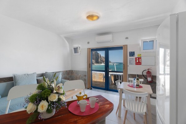 A dining area with a table, chairs, a flower arrangement, and a view of the sea through a glass door.