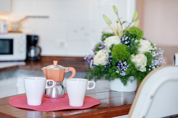 Un comptoir de cuisine avec une machine à café, deux tasses blanches et un arrangement floral.
