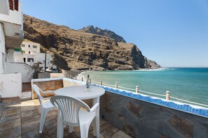Une terrasse avec une table et des chaises, donnant sur une zone côtière avec une falaise rocheuse et la mer.