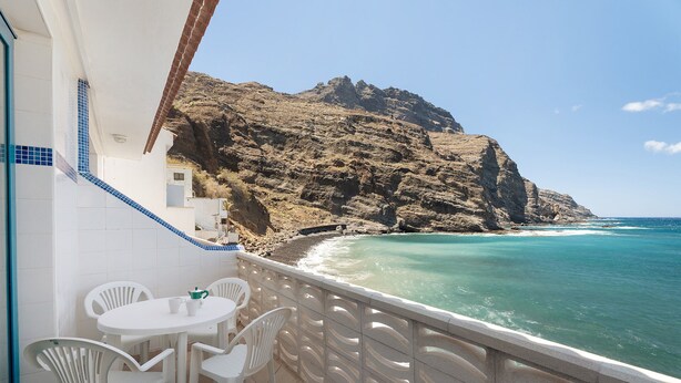 A balcony with white chairs and a table, overlooking a rocky coastline and turquoise sea. - Apartment 'Playa Azul - 7' with Sea View, Private Terrace and Wi-Fi (Vallehermoso)