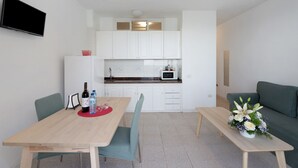 A compact living space with a dining table, chairs, a sofa, a kitchenette, and a flat-screen TV. - Apartment 'Playa Azul - 7' with Sea View, Private Terrace and Wi-Fi (Vallehermoso)