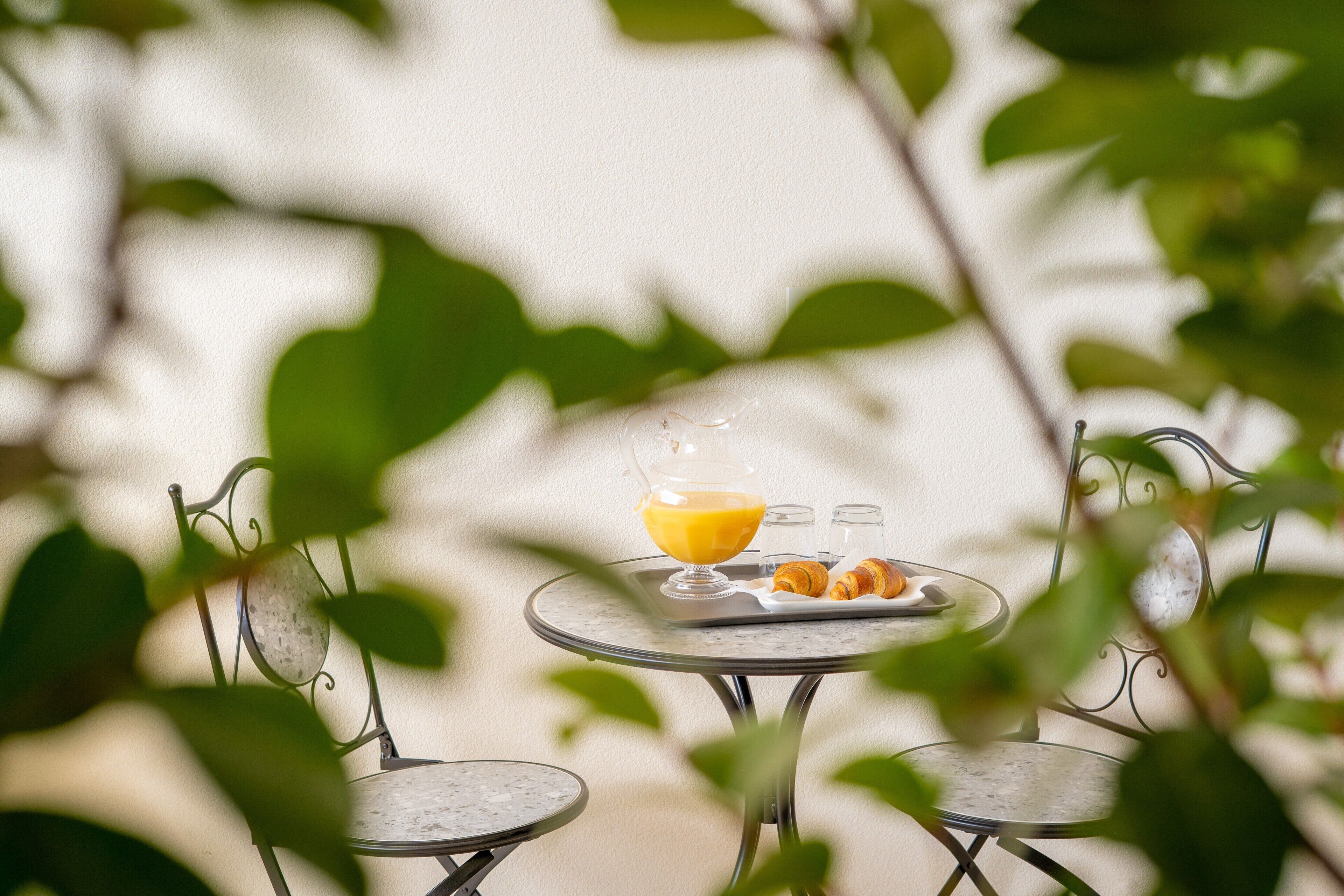 Une table avec un verre de jus d’orange et des croissants, entourée de chaises en métal.