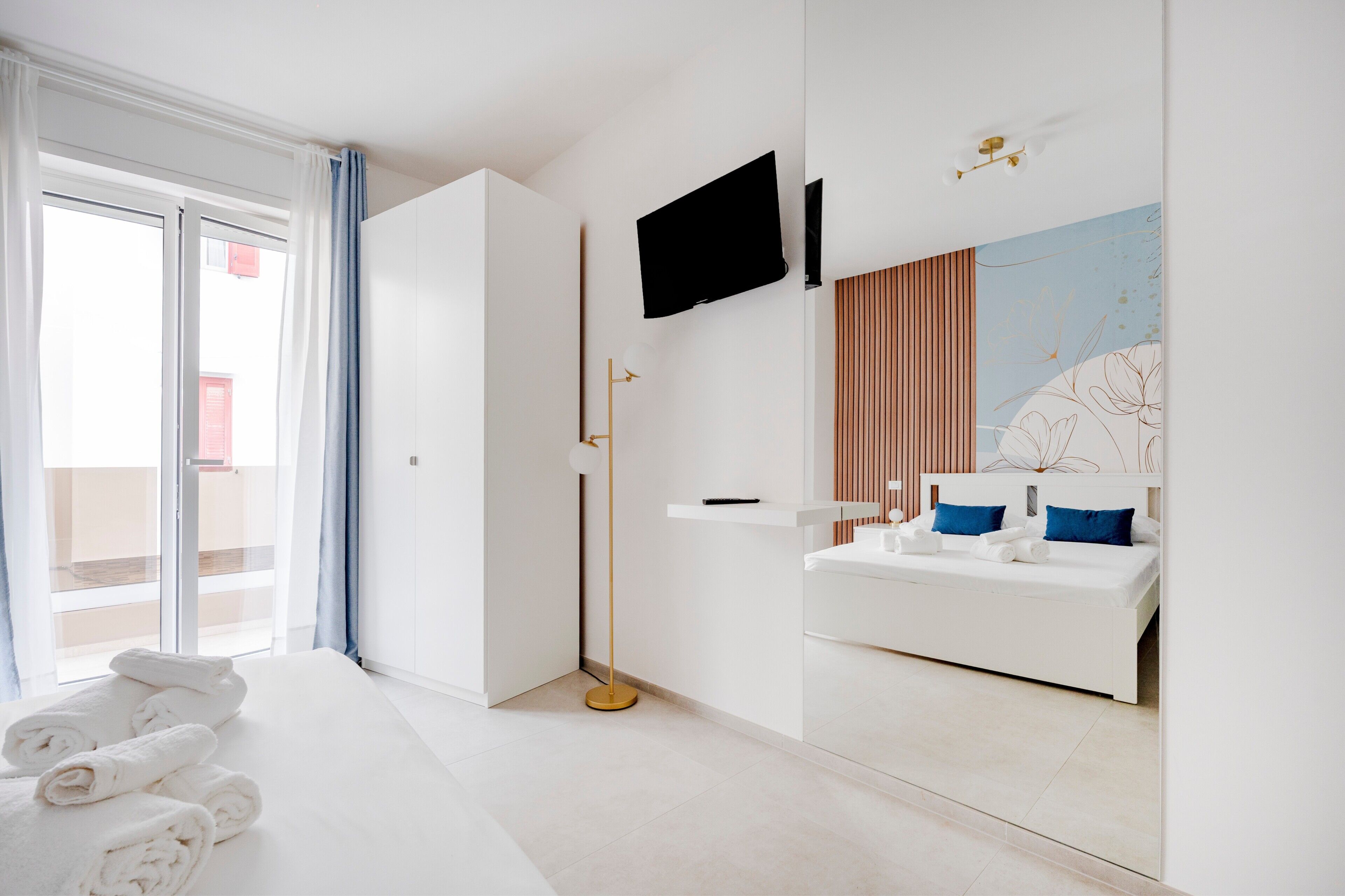 Ein modernes Hotelzimmer mit einem Bett, einem großen Spiegel, einem Flachbildfernseher und einem Nachttisch.