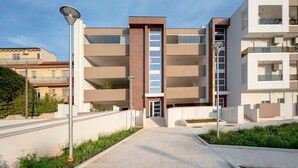 A modern multi-story residential building with a central staircase, balconies, and a paved walkway. - Room 'Volutta' with Shared Terrace, Wi-Fi and Air Conditioning (Conversano)