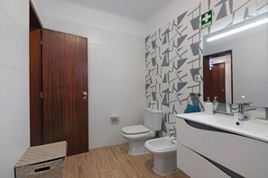 Un baño con puerta de madera, paredes de azulejos blancos y un diseño decorativo, un lavamanos blanco y un bidé.