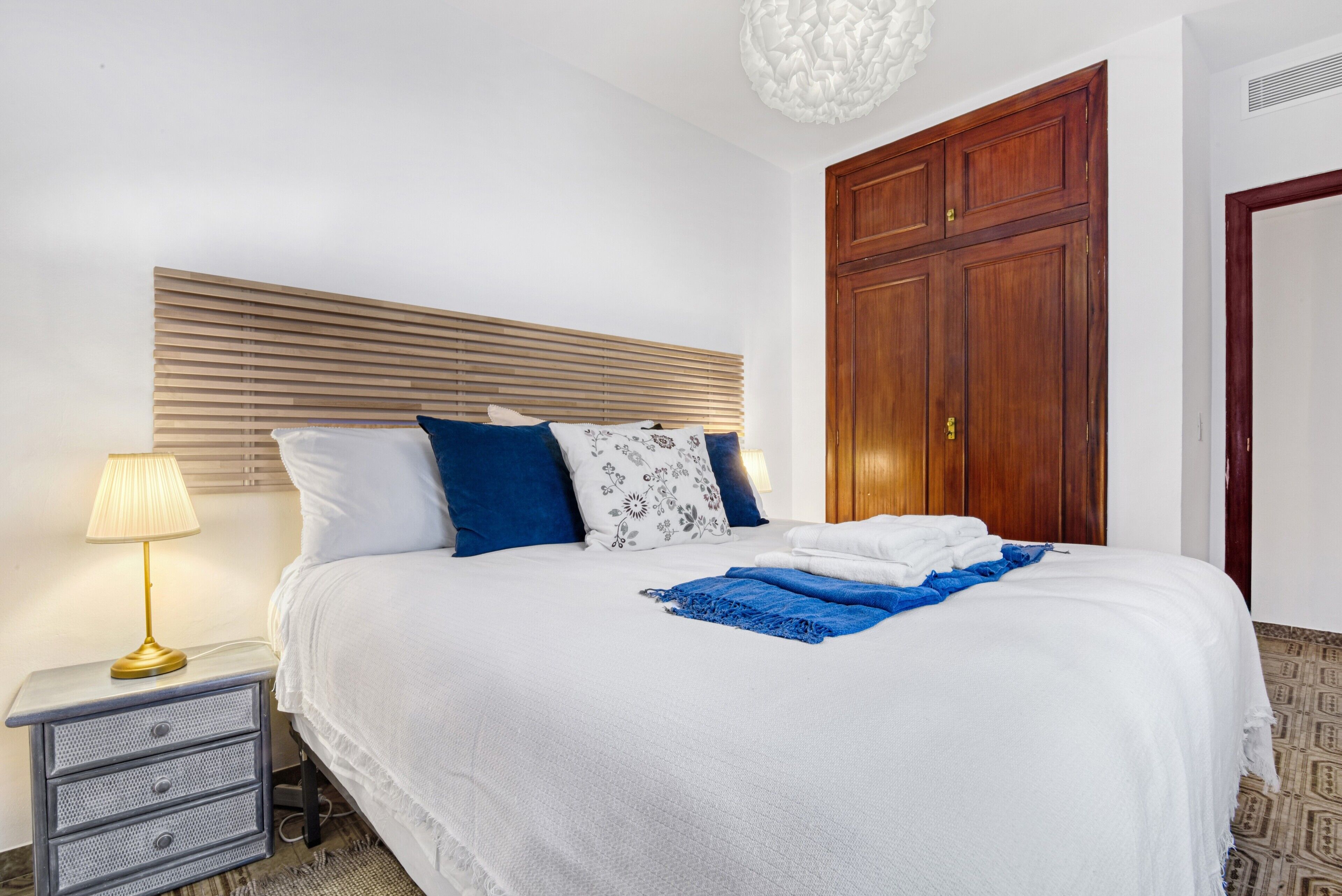 A neatly made bed with a white and blue bedspread, a blue throw blanket, and a gold lamp on a bedside table.