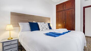 A neatly made bed with a white and blue bedspread, a blue throw blanket, and a gold lamp on a bedside table.
