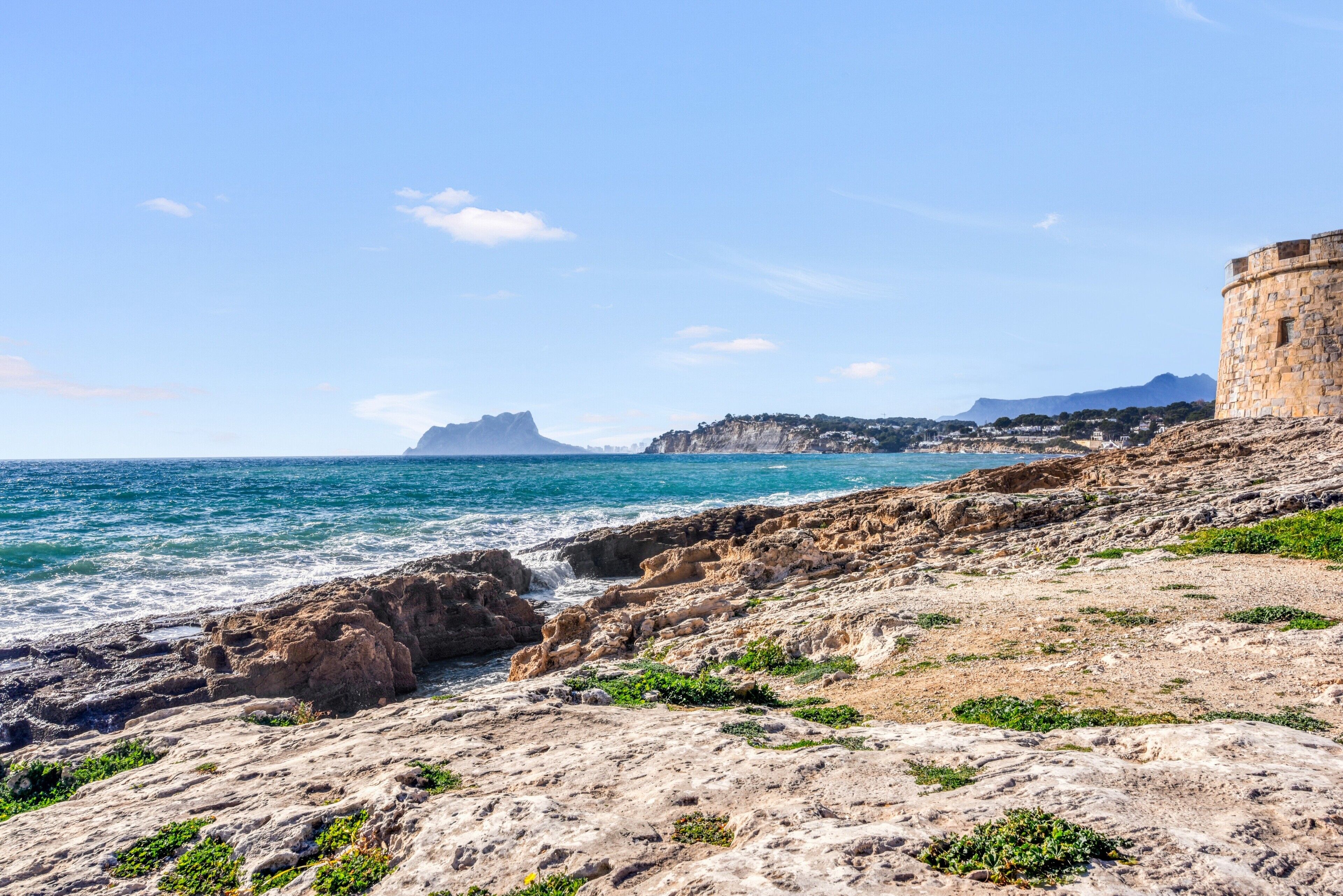 A coastal landscape with rocky terrain, a stone building, and a distant mountain.