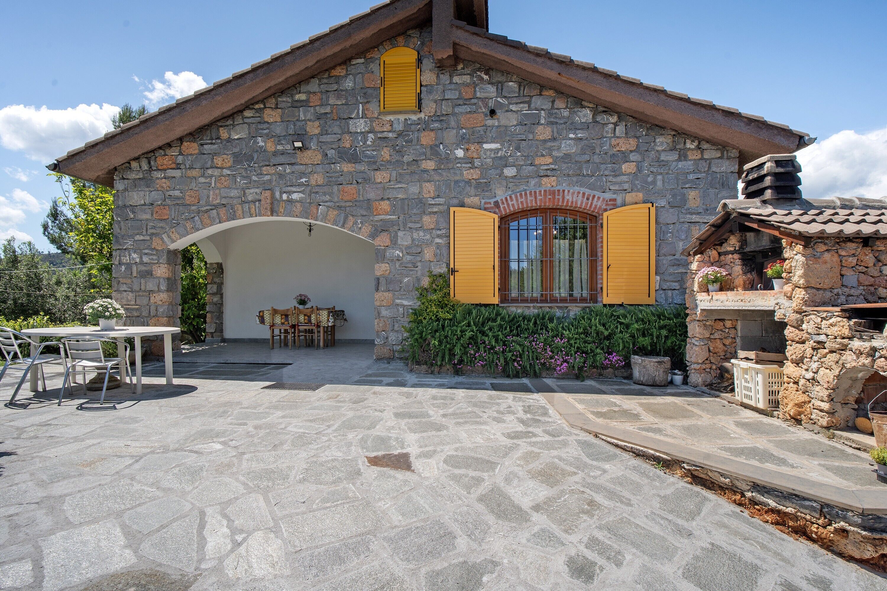 Un bâtiment en pierre doté d’un patio couvert, de sièges en plein air et d’une cheminée en pierre.