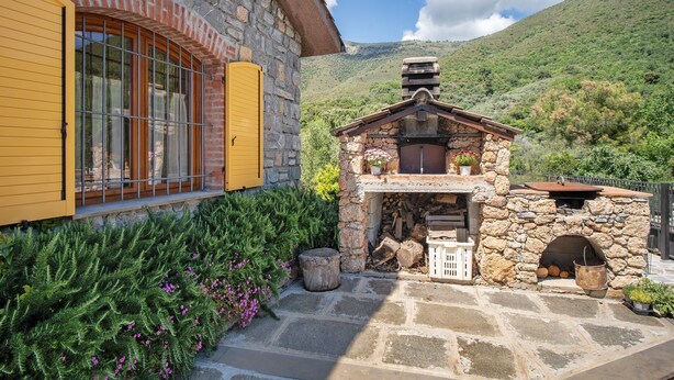 Un edificio de piedra con una puerta amarilla y ventanas, una chimenea de piedra y vistas a una ladera verde.