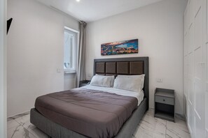 A bedroom with a bed, a nightstand, a window, and a painting on the wall.