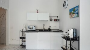 Eine moderne Küche mit weißen Schränken, einer schwarzen Arbeitsplatte, einer eingebauten Mikrowelle, einer Kaffeemaschine und einem kleinen Regal mit Küchenutensilien.