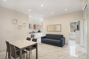 A modern living space with a dining area, a sofa, a kitchen, and a large mirror.