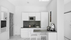 Una cocina moderna con armarios blancos, salpicadero de mármol, microondas integrado, cafetera y lavamanos.
