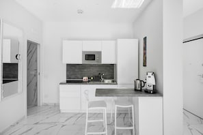 A modern kitchen with white cabinetry, a marble backsplash, a built-in microwave, a coffee maker, and a sink.