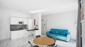 Una cocina moderna con armarios blancos, una mesa redonda de madera y un sofá azul en un espacio luminoso.
