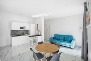 A modern kitchen with white cabinets, a round wooden table, and a blue sofa in a bright living area.