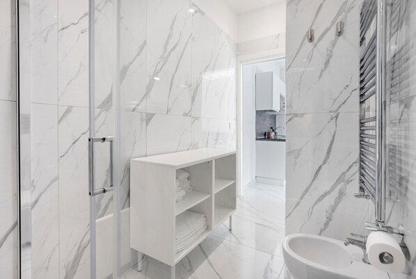 Un baño moderno con paredes de mármol, cabina de ducha de vidrio, tocador blanco y un inodoro.
