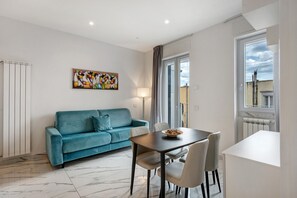 A modern living room with a teal sofa, a dining table, and a painting on the wall.