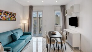 Una sala de estar moderna con un sofá, mesa de comedor, sillas, televisor y un cuadro en la pared.