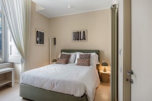 A bedroom with a bed, two pillows, a bedside table, a lamp, and two wall-mounted signs.