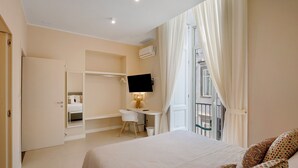 A bedroom with a bed, a desk, a chair, a TV, and a balcony with curtains. - Room 'San Severo' with Balcony, Wi-Fi and Air Conditioning (Napoli)