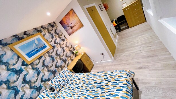 A bedroom with a bed, a desk, a chair, and a painting on the wall.