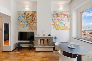 Een moderne woonkamer met een open haard, een flatscreen televisie, een eettafel en twee grote abstracte schilderijen.