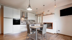 A modern kitchen with white cabinets, a built-in oven, and a dining area with a wooden table and chairs. - Apartment 'Mimosa' with Shared Garden and Air Conditioning (Pitigliano)