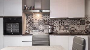 A modern kitchen with a built-in oven, a coffee machine, and a patterned backsplash. - Apartment 'Mimosa' with Shared Garden and Air Conditioning (Pitigliano)