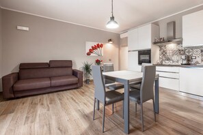Una cocina moderna con armarios blancos, una mesa de comedor con sillas y un sofá marrón en la sala.