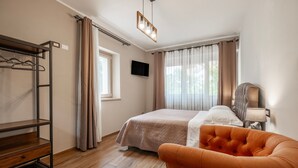 A hotel room with a bed, a chair, a TV, a shelf, and a window with curtains. - Apartment 'Mimosa' with Shared Garden and Air Conditioning (Pitigliano)