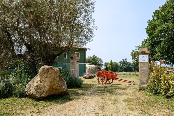 A rustic outdoor area with a stone pathway, a wooden cart, and a green building with a tiled roof.