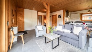 A wooden interior with a sofa, chairs, a table, and a kitchen area. - Cottage 'Côté Giffre' with Lake View, Private Terrace and Wi-Fi (Châtillon-sur-Cluses)