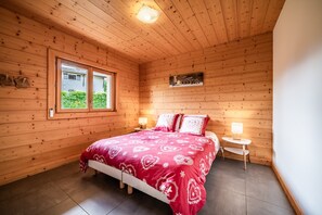 Ein Zimmer mit Holzwänden, einem Bett, Nachttischen, einem Fenster und einem Wandbild.