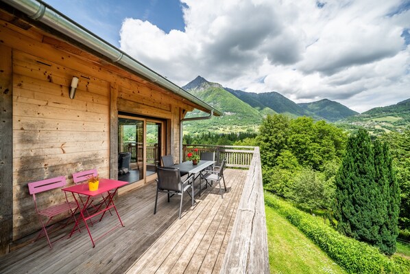 Eine Holzdielen-Terrasse mit Tisch und Stühlen mit Blick auf eine gebirgige Landschaft.