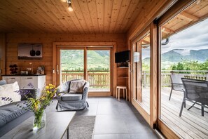 En inredning med träpanel, en soffa, ett bord med en vas med blommor, en tv och utsikt över bergen genom stora skjutdörrar.