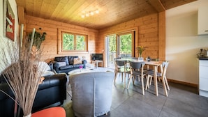 Een houten blokhut van binnen met een zithoek, een eethoek en een keuken.