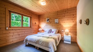 Een kamer met houten lambrisering, een bed, twee nachtkastjes met lampen en een raam met uitzicht op groen.