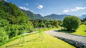 Een gazon met een schommel, een stenen muur en een bergachtig landschap op de achtergrond.