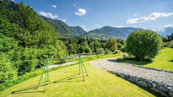 Un'area verde con altalene, un muro in pietra e montagne sullo sfondo.