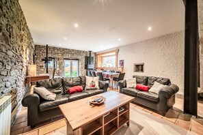 A cozy living room with stone walls, leather sofas, a wooden coffee table, and a dining area with a stone fireplace.